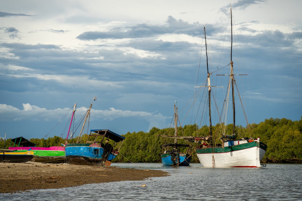 portfolio-06 Scenic view of vibrant boats docked on a sandy shore in Madagascar, under a dramatic sky.